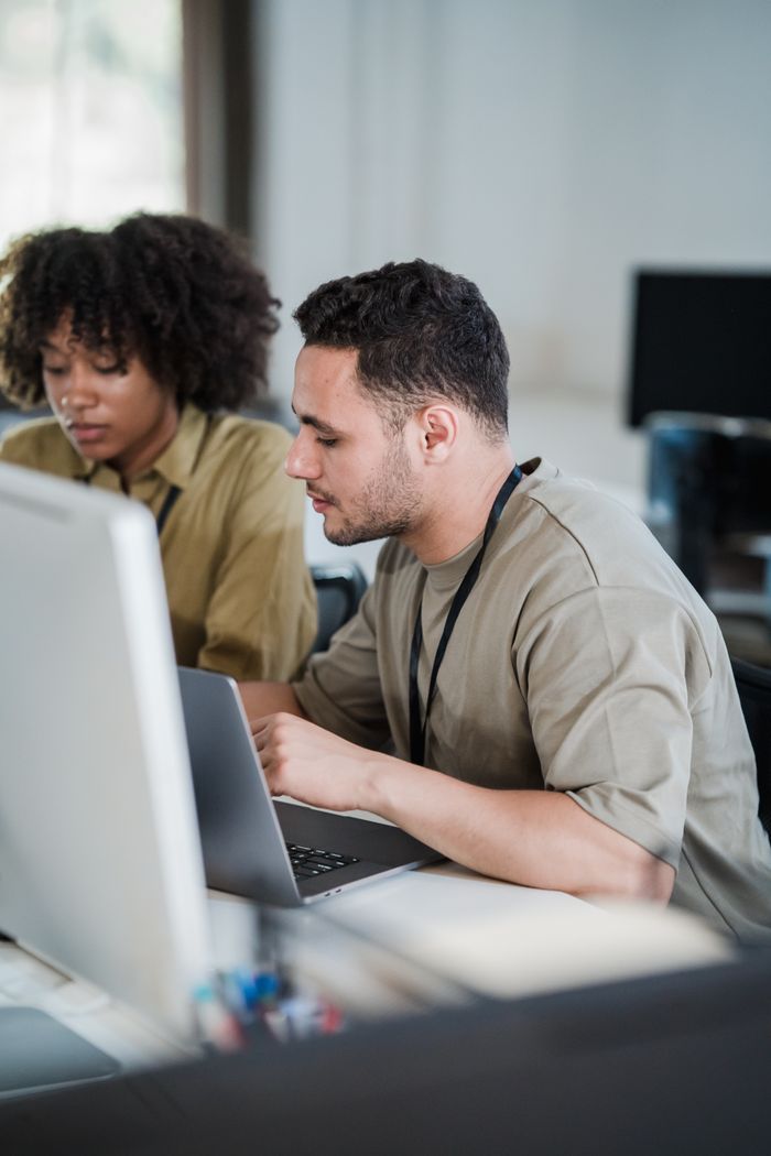Two office workers collaborate on a computer task, working efficiently in a modern office setting.
